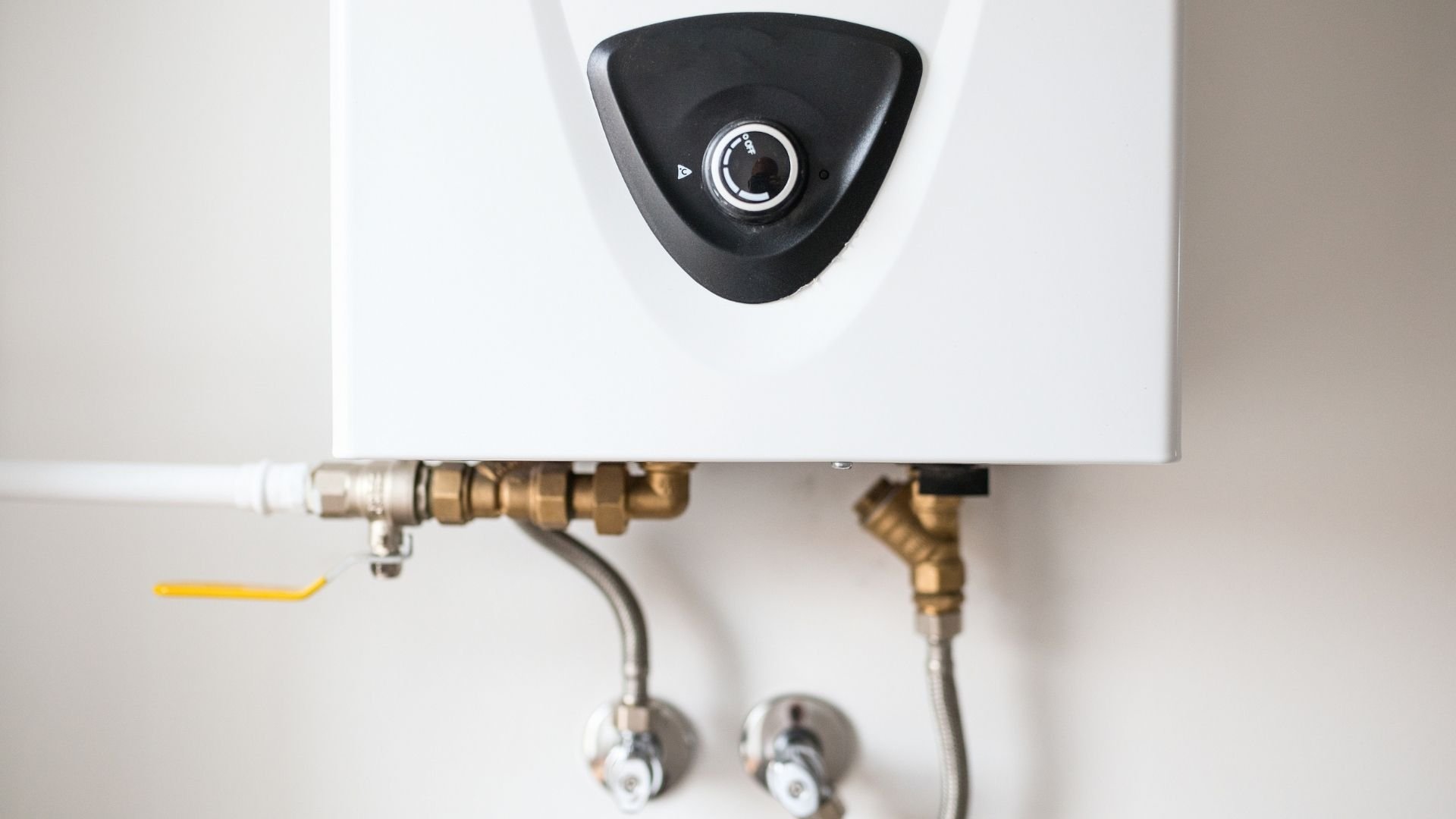 White water heater with black control panel and brass pipe connections